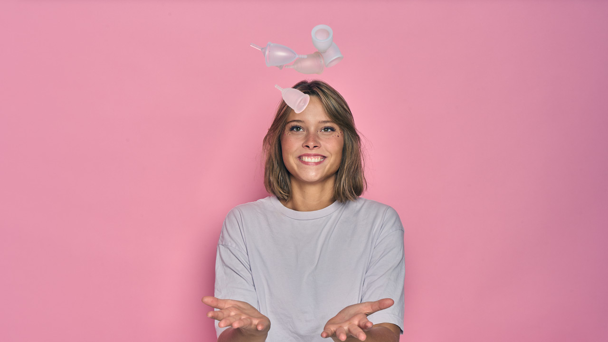Een persoon jongleert met menstruatie cups met een roze achtergrond