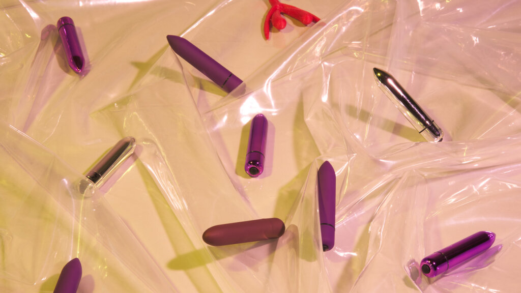 Et utvalg av klitorisvibratorer som ligger på gjennomsiktig plastikk på en beige bakgrunn
