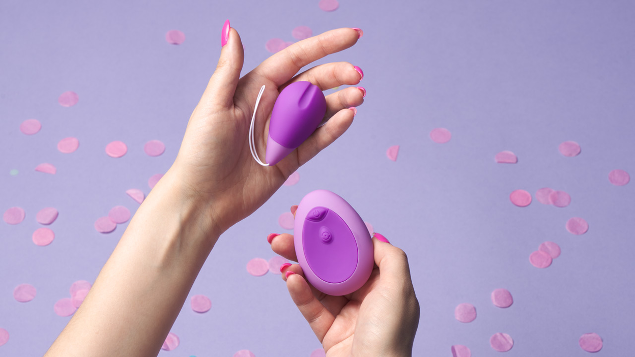 Zwei Hände halten ein lilafarbenes Sexspielzeug mit Fernbedienung
