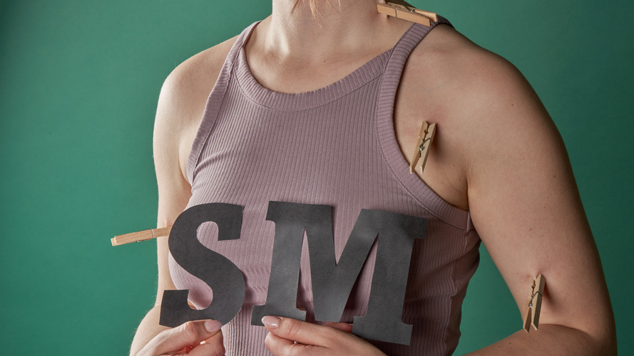 Person with clamps on their arms holding the letters SM