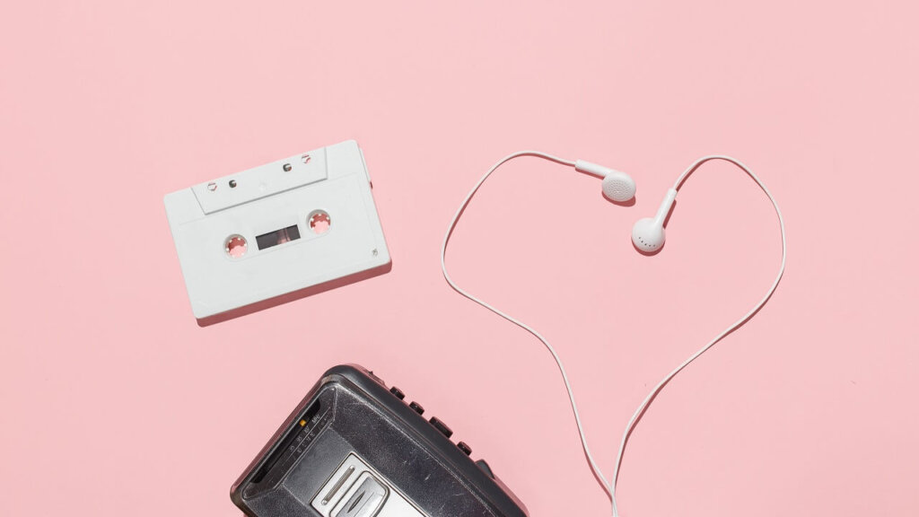 En båndoptager, et kassettebånd og et par høretelefoner på en lyserød baggrund