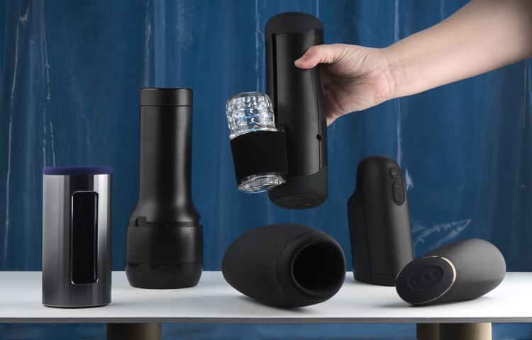 A hand holds a black piece of sex toy while five other products are placed on a table