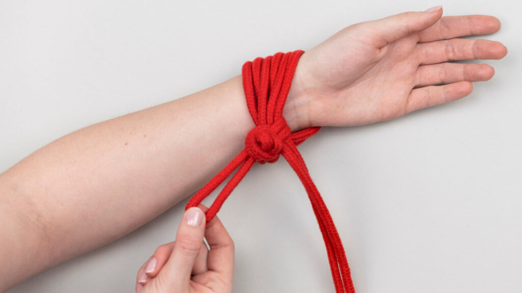 Hånd som knyter en knute med bondage tau rundt et håndledd