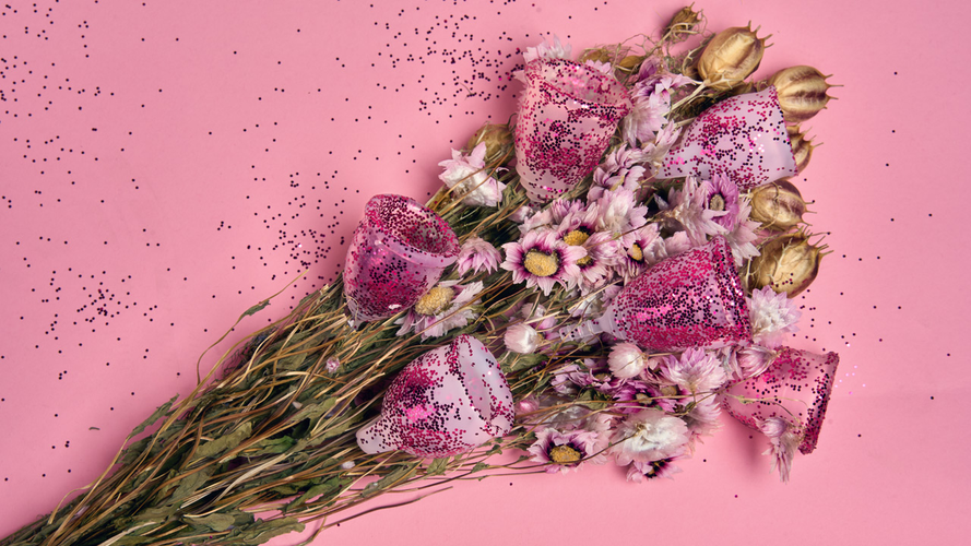Menstrual cups with glitter in a bouquet of flowers on a pink background