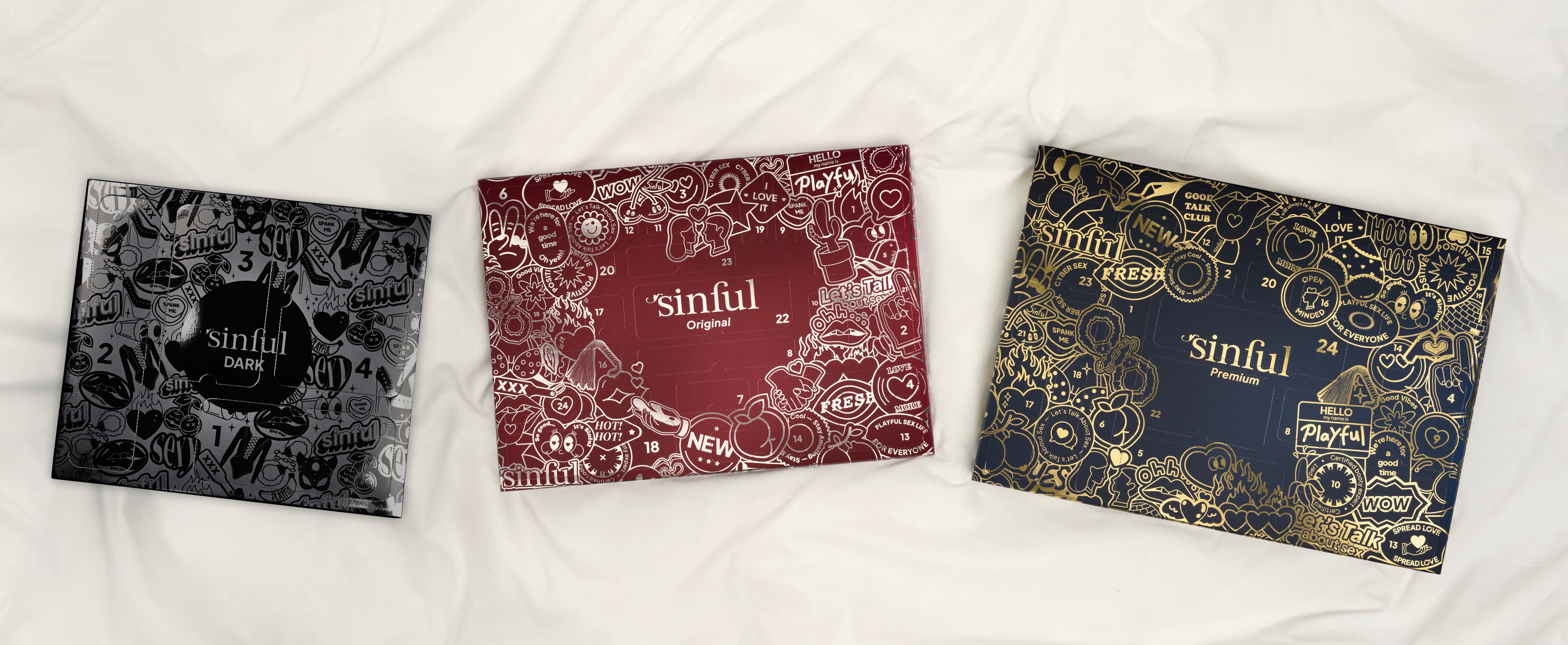 Drei Sinful-Adventskalender nebeneinander auf einem weißen Laken.
