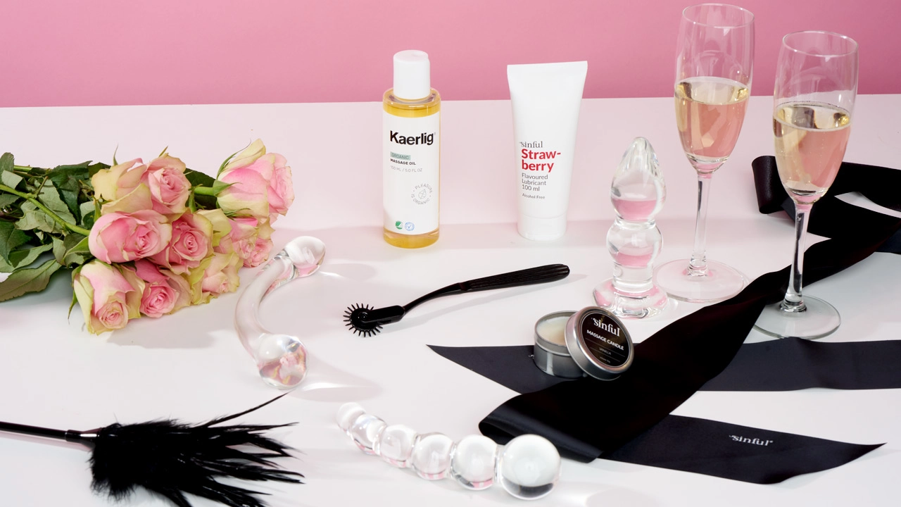 Sexlegetøj, massageolie, glidecreme, blomster og champagneglas på et bord