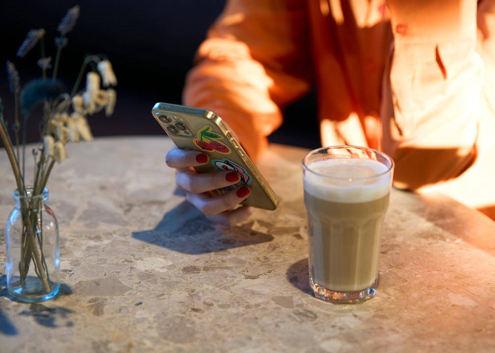 Tafel met een café latte en een hand die een telefoon vast houdt.