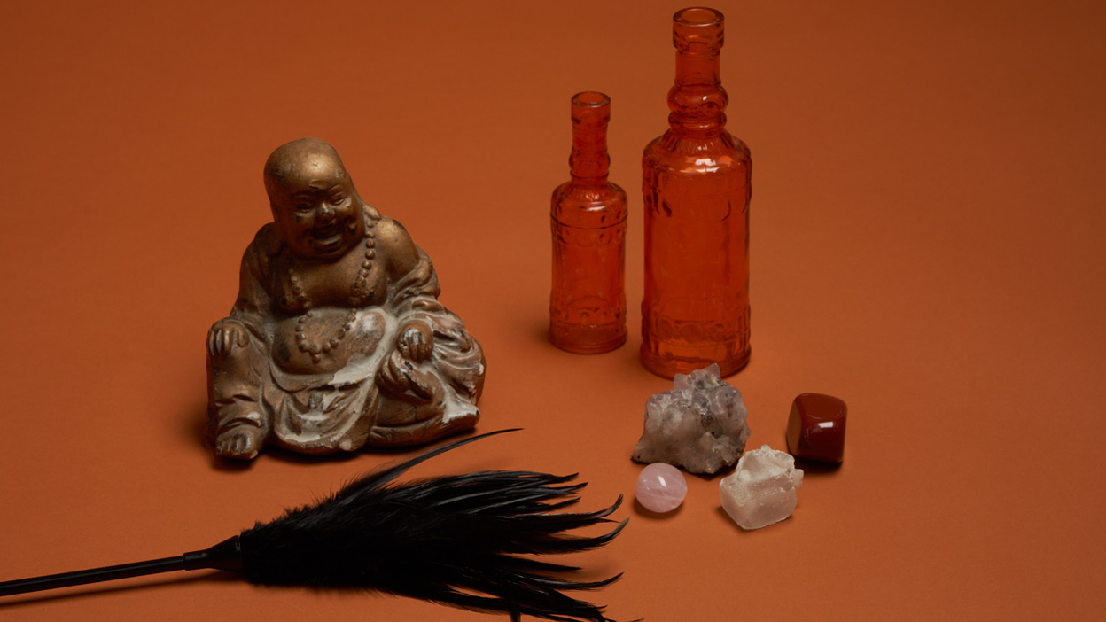 A tickling feather, a Buddha figure, two bottles, and small crystals standing together