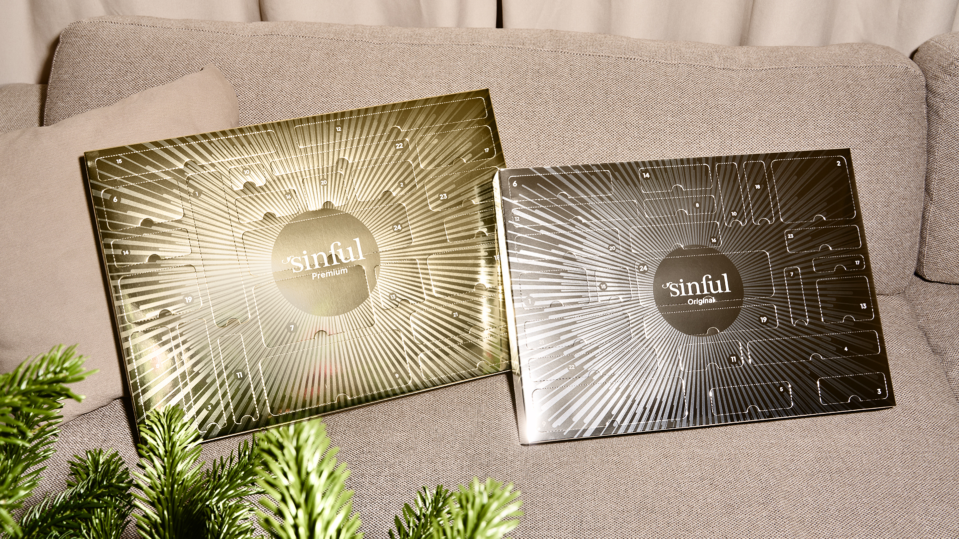 Sinful Premium- och Original-julkalendrar uppställda på en soffa bredvid en julgran