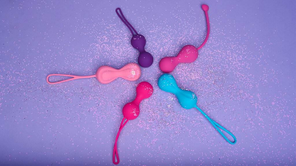 Five kegel balls in different colours on a light purple background with glitter