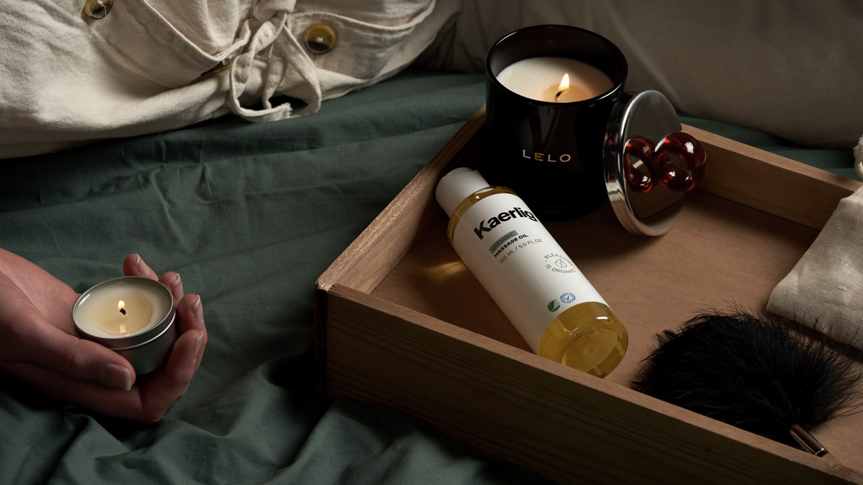 A lit Lelo massage candle, massage oil, and a tickling feather lying in a wooden tray