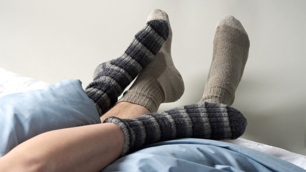 Füße von zwei Personen, die unter einer Bettdecke hervorschauen