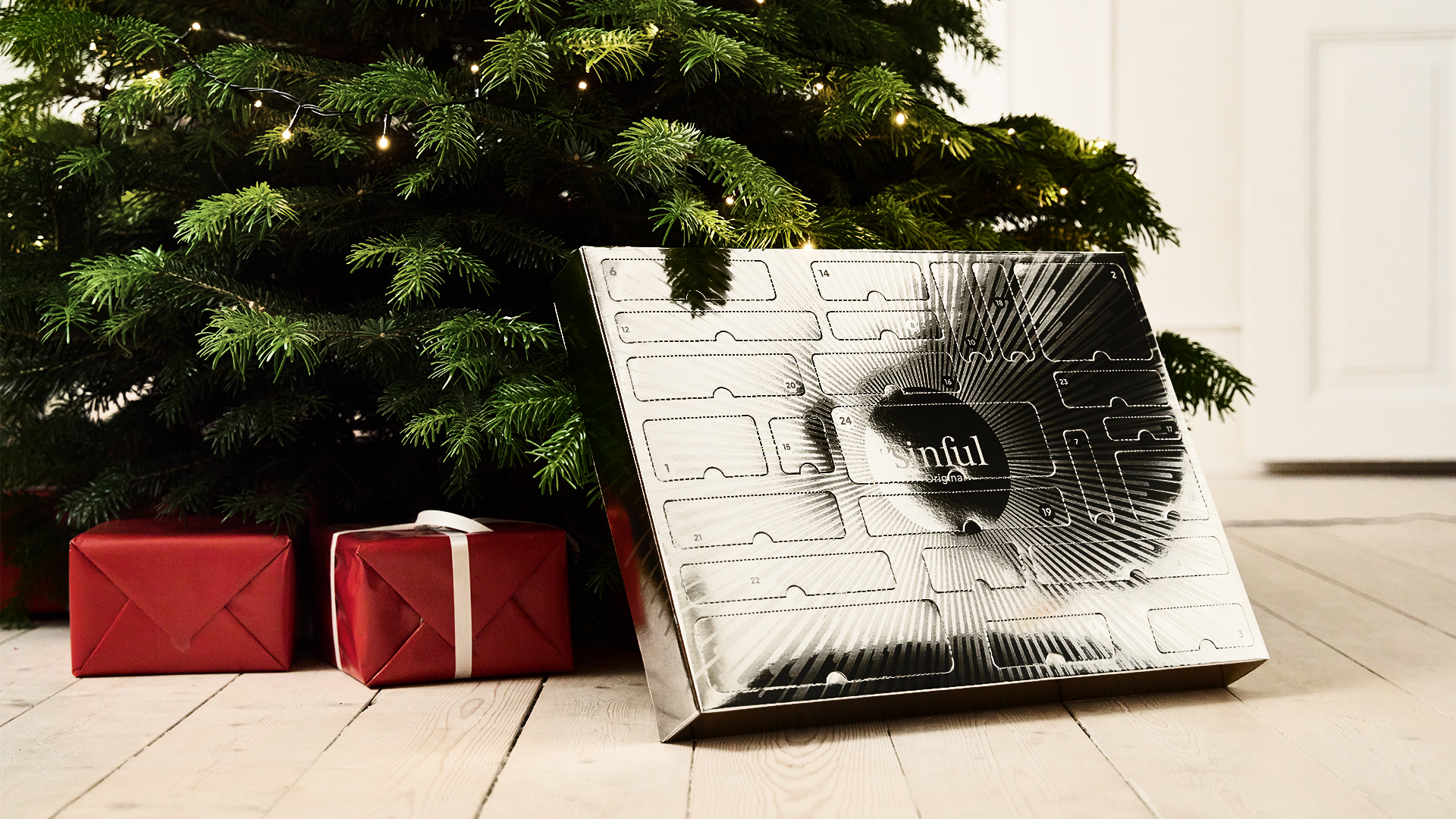 Sinful Original-adventskalender och inslagna julklappar utställda under en upplyst julgran