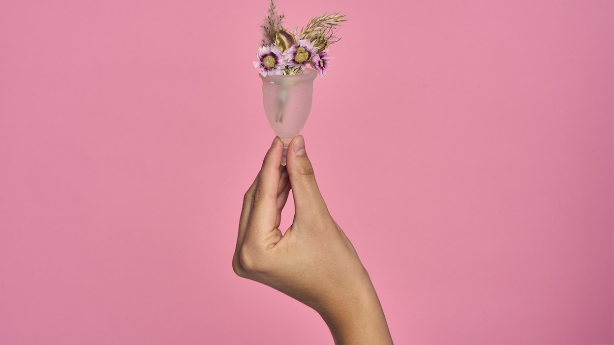 Een hand houdt een menstuatie cup met bloemen erin vast
