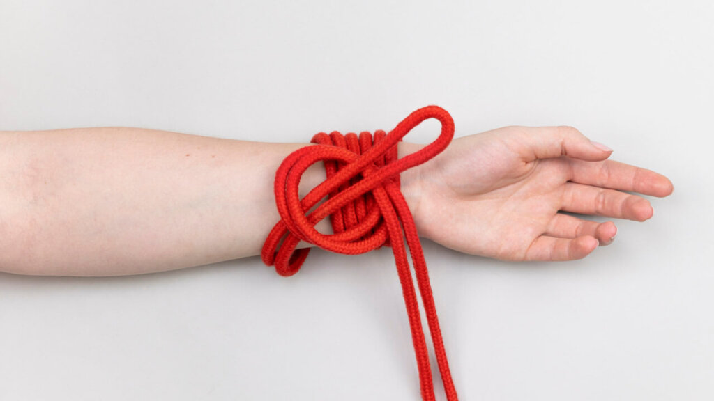 Corde de bondage enroulée sur un bras au milieu du processus de faire un nœud