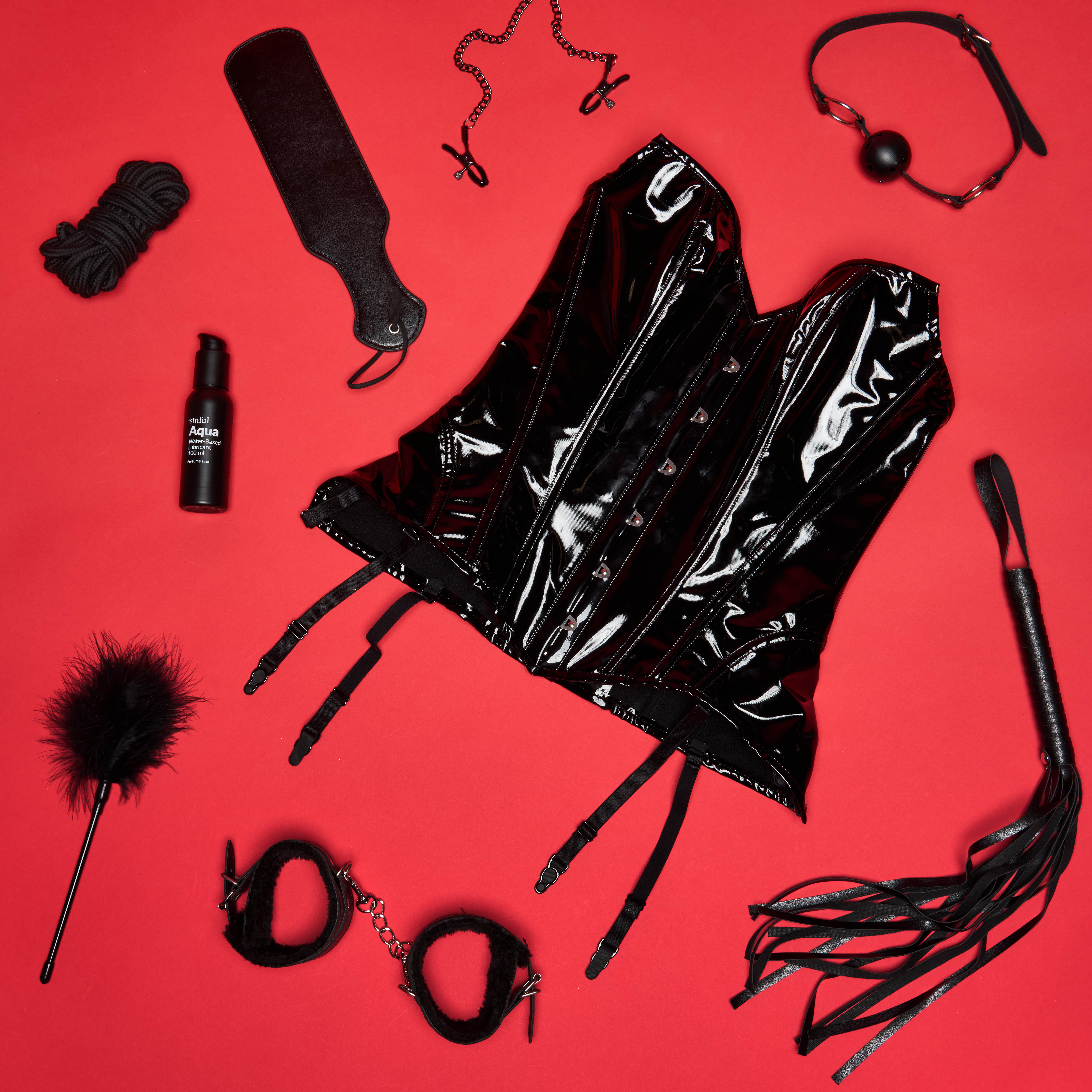 Een zwart korset met seksspeeltjes en glijmiddel op een rode achtergrond