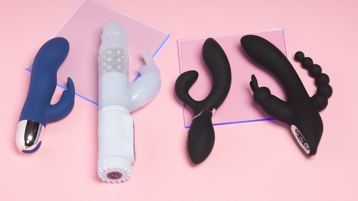 Two black, one white and one blue rabbit vibrator lying next to each other on a pink background