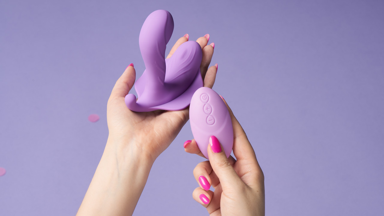Kaksi kättä, jotka pitelevät violettia seksilelua kaukosäätimellä