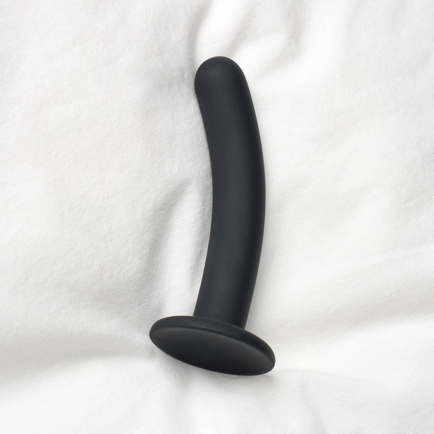 A strap-on dildo with suction cup lying on a bed sheet