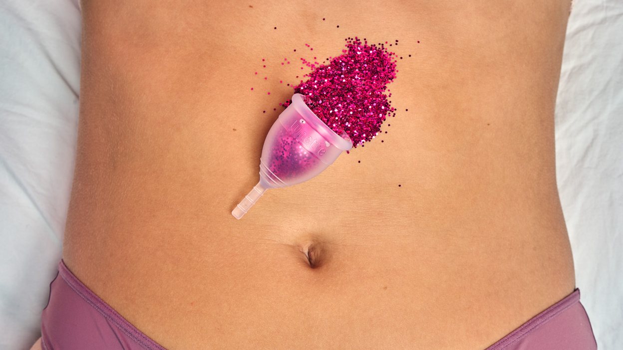 Eine Menstruationstasse mit Glitter liegt auf einem nackten Bauch