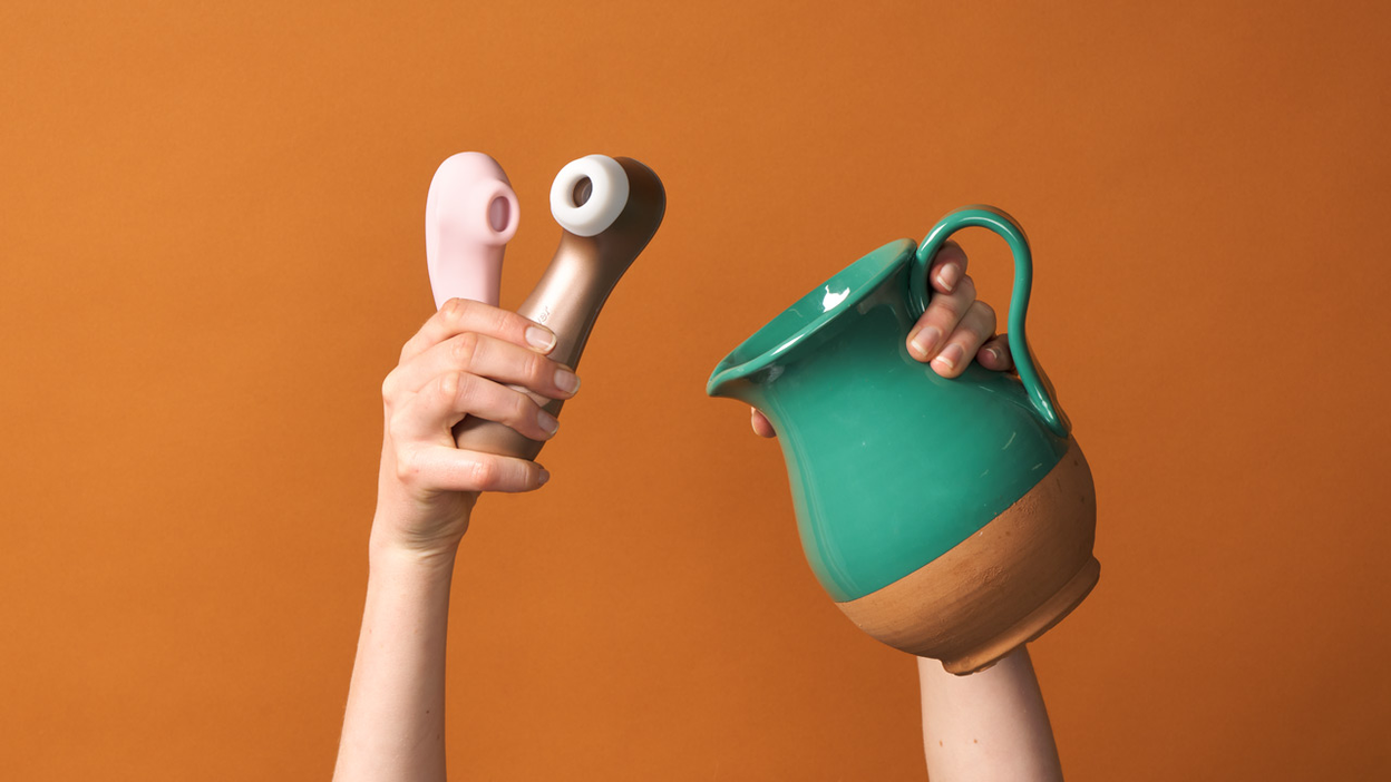 Hands holding two clitoral stimulators and a jug