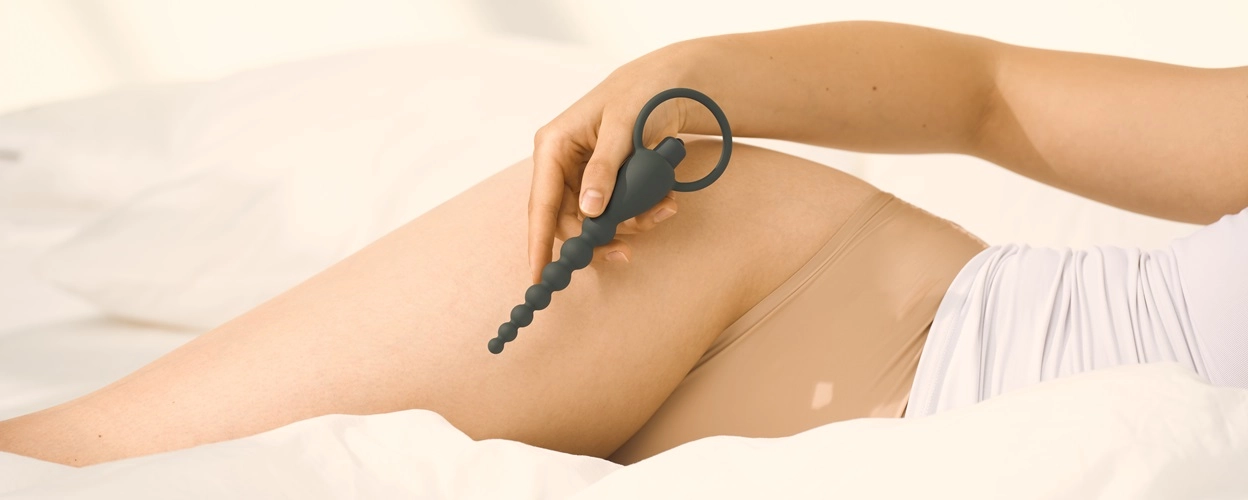En kvinde ligger i sengen og holder en analvibrator