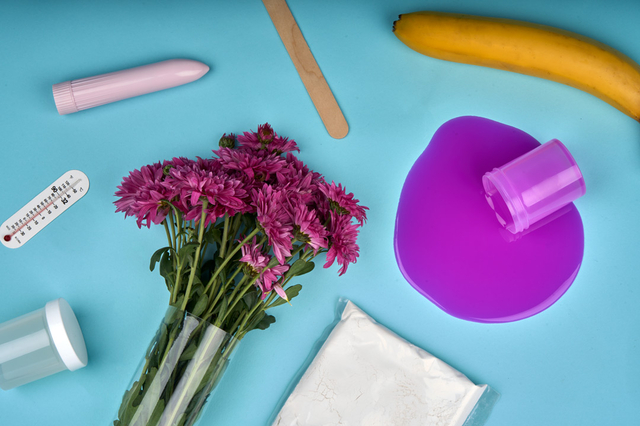 En blomsterbuket og diverse produkter fra et Clone A Willy sæt ligger på en blå baggrund