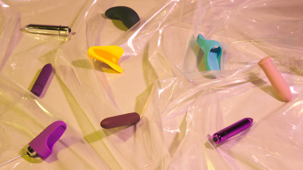 Små vibratorer i forskjellige farger som ligger på gjennomsiktig plastikk på en beige bakgrunn