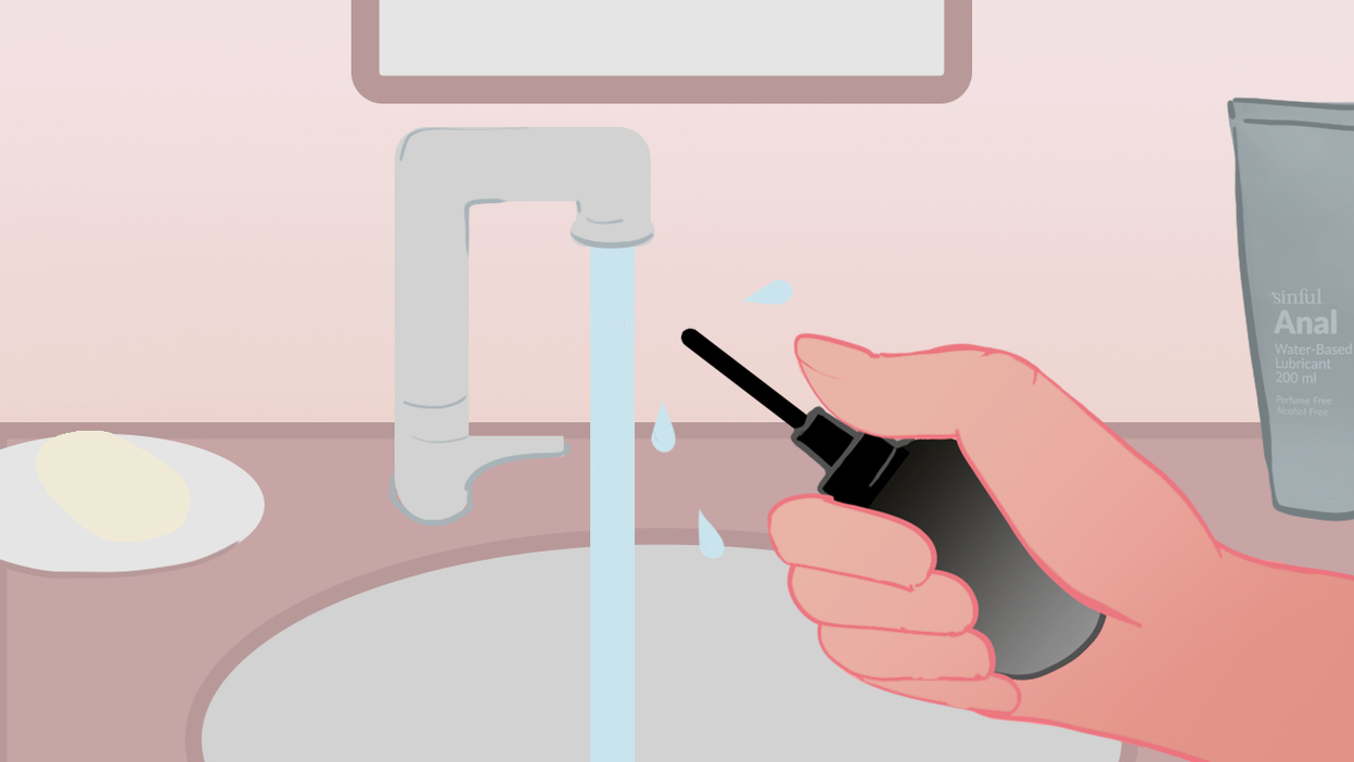 Illustration einer Hand, die eine schwarze Analdusche unter einem Wasserhahn hält