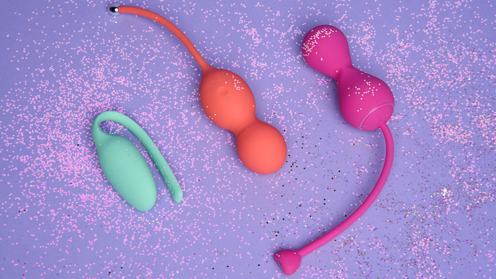 Three kegel balls in different colours on a light purple background with glitter