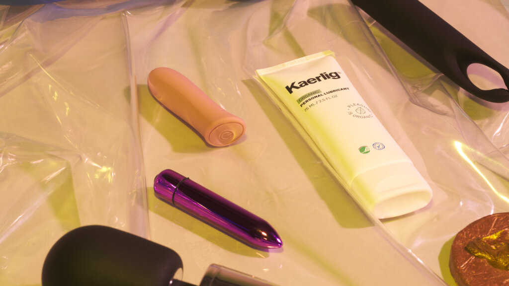 En Kaerlig glidecreme og vibratorer til klitoris ligger på gennemsigtigt plastik på en beige baggrund