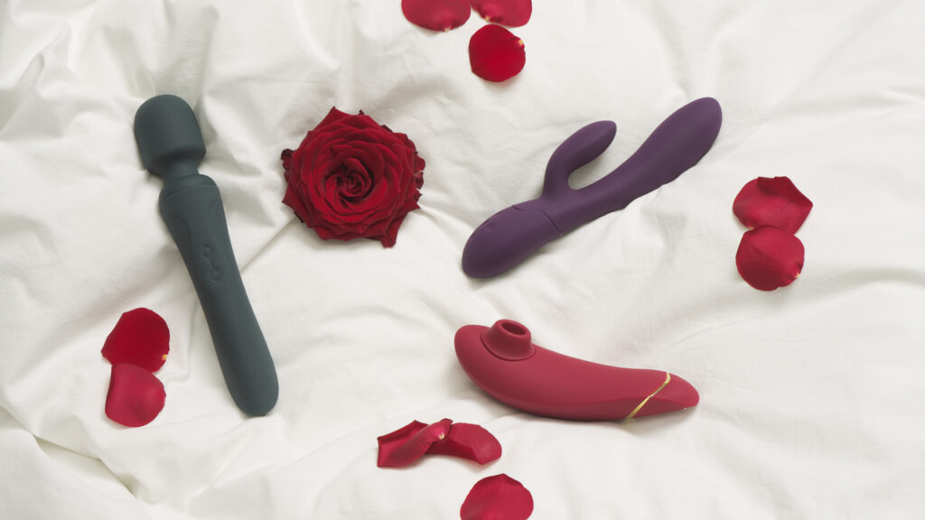 Three sex toys, a rose and rose petals lie next to each other on a bed
