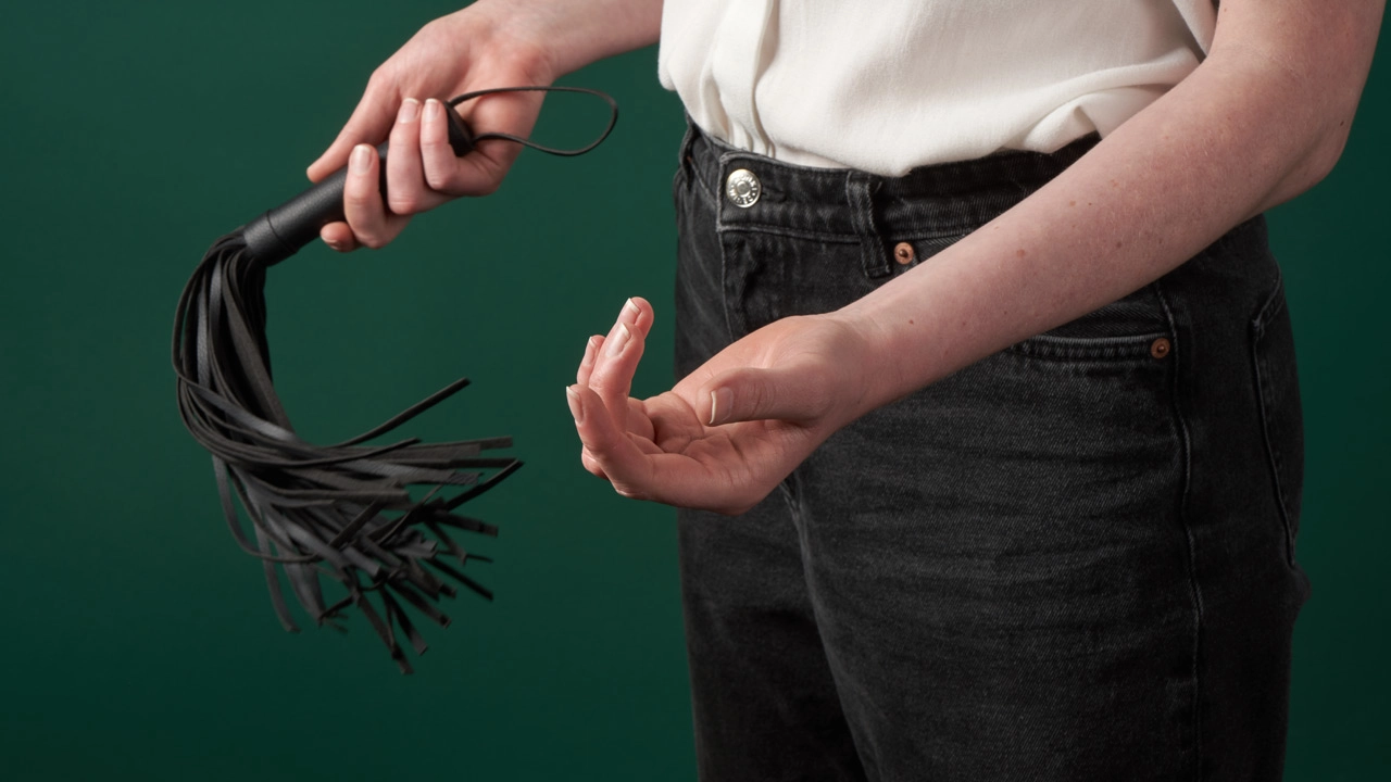 Person med BDSM flogger i den ene hånden
