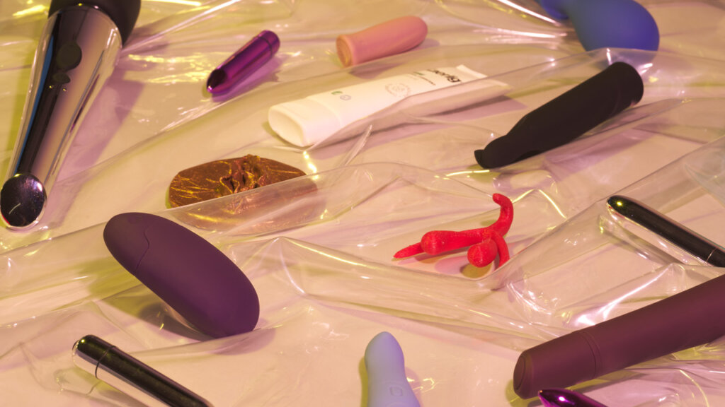 Diverse produkter til klitoris som ligger på gjennomsiktig plastikk på en beige bakgrunn