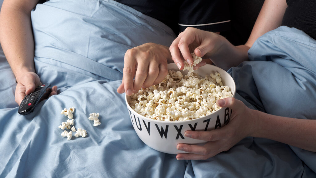 En skål med popcorn i en säng med två händer som tar popcorn