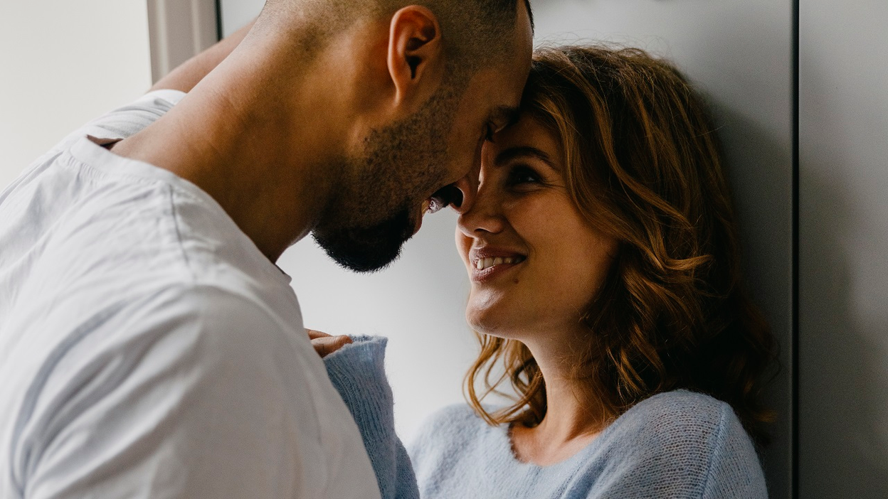 A man and a woman stand close together while looking into each other's eyes