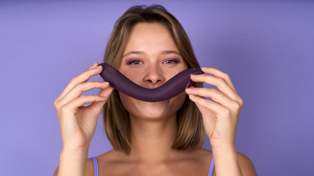 Een vrouw houd een paars seksspeeltje voor haar mond