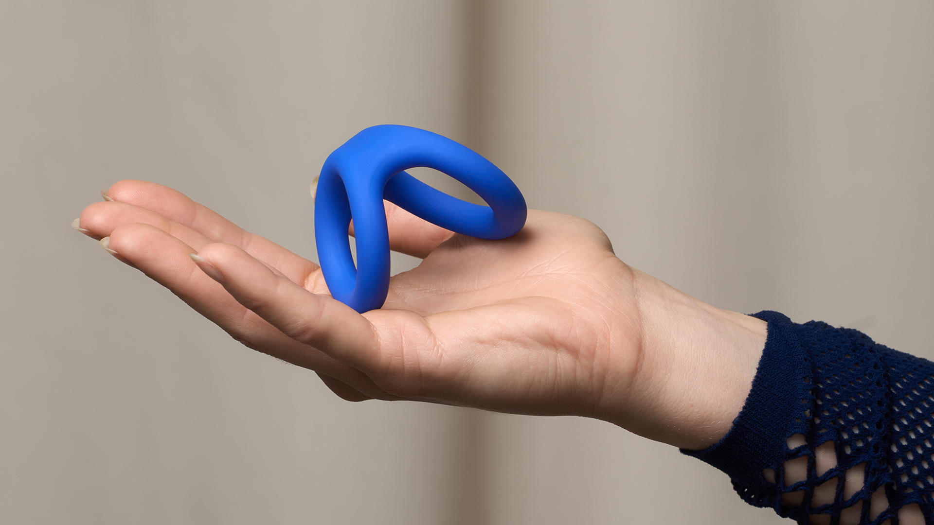 En hand som håller en blå, elastisk dubbel penisring