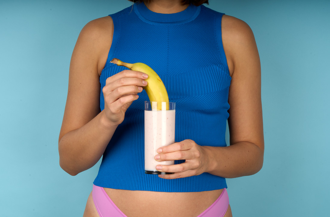 Person doppar en banan i ett glas yoghurt som de håller framför sig