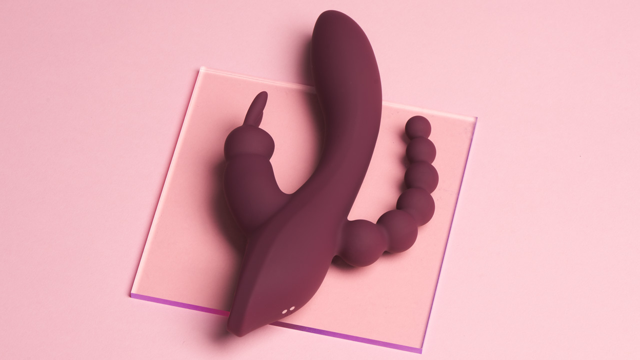 Bordeauxfarbenes Sexspielzeug liegt auf einer Glasplatte auf einem rosa Hintergrund