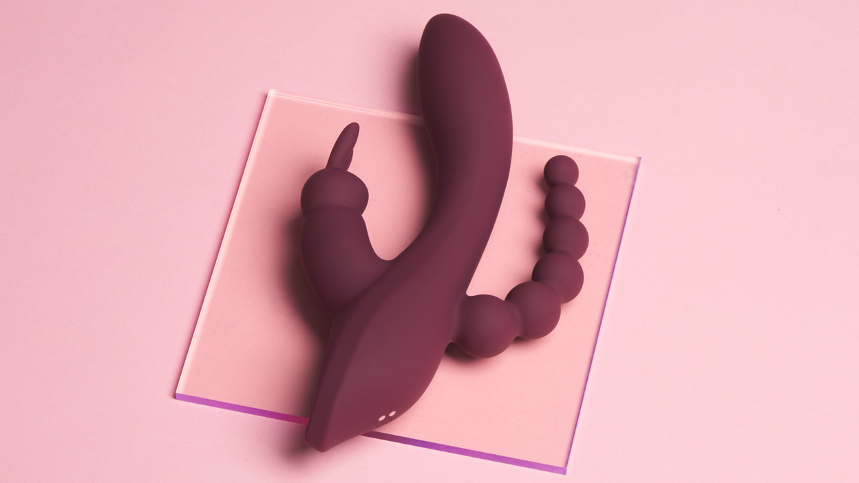 Sextoy de couleur bordeaux posé sur une plaque de verre sur fond rose