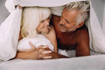 Mies ja nainen halailevat sängyssä hymyillen 