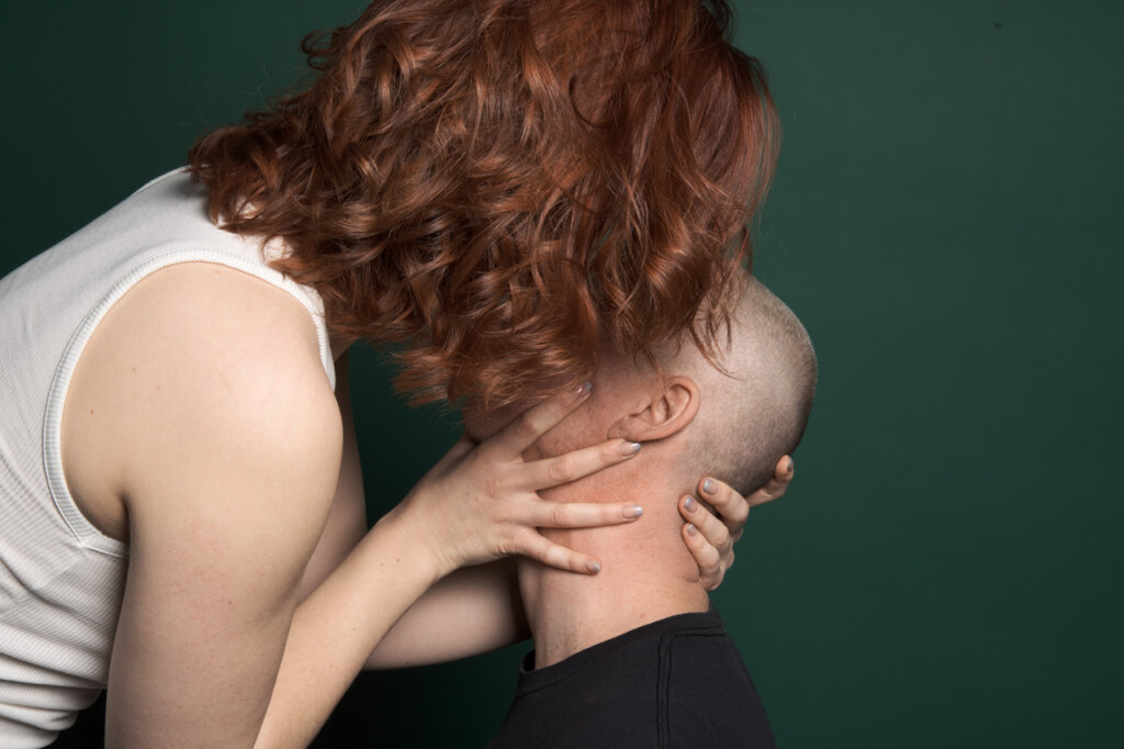 A woman and a man being very close to each other while she’s holding his head