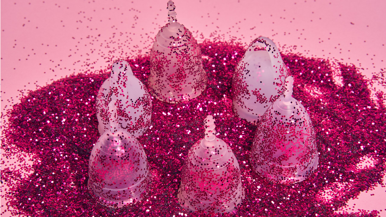 Sechs Menstruationstassen mit Glitzer liegen auf einem rosa Hintergrund