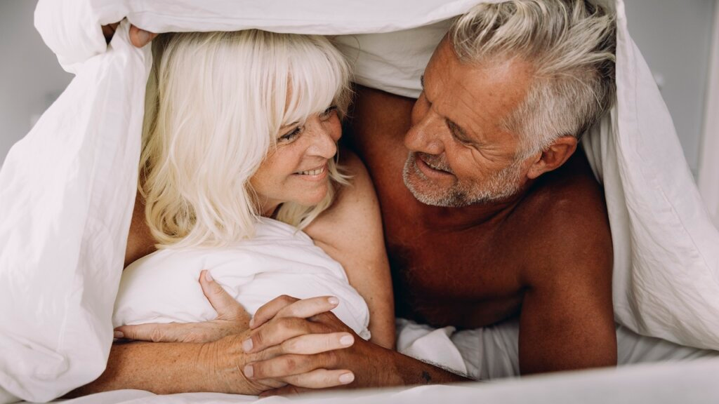 older couple lay side by side smiling while one puts their arm around the other