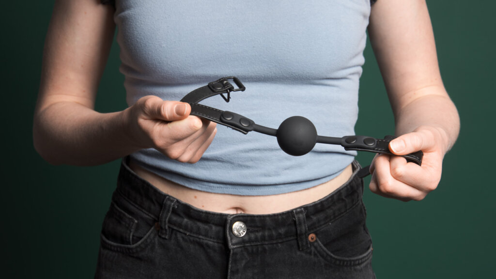 Woman standing with a ball gag in her hands