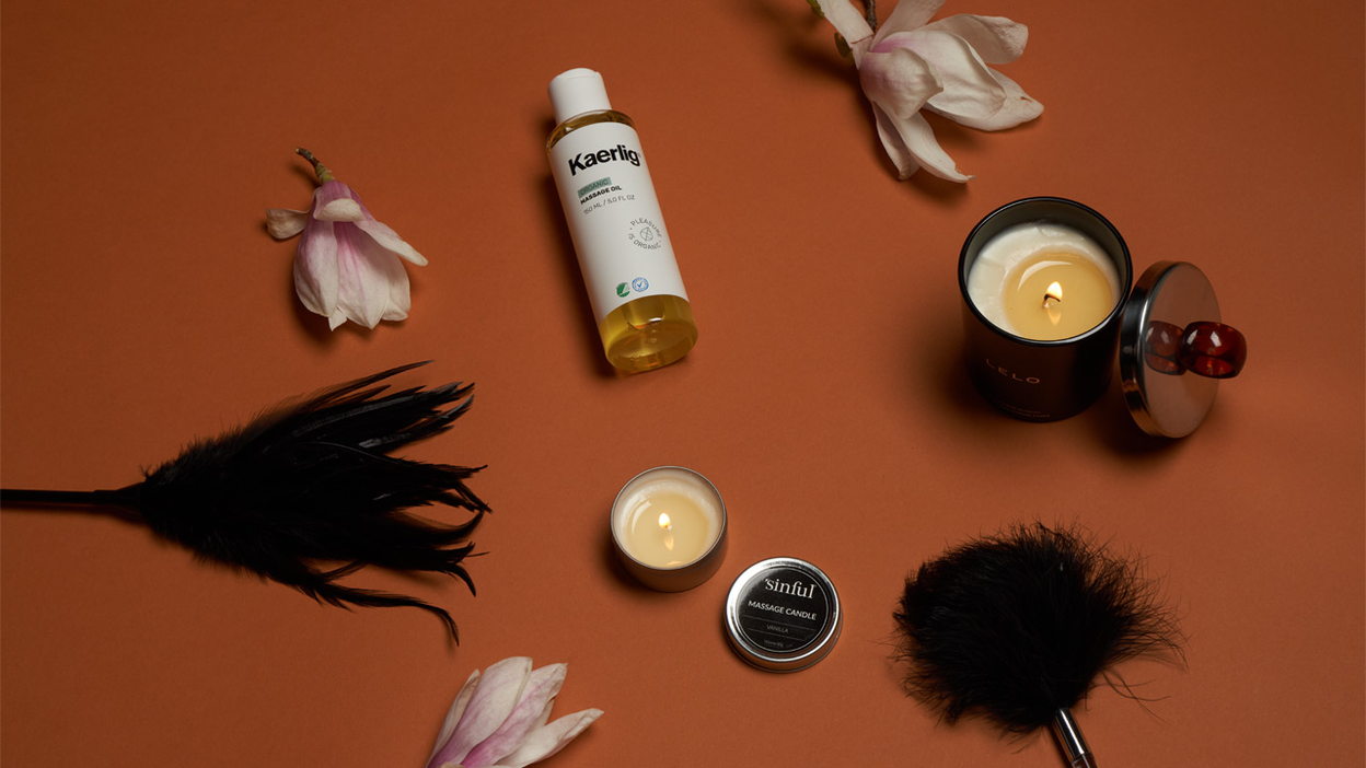 Des bougies de massage, de l'huile de massage, des plumes et des petites fleurs sur fond orange