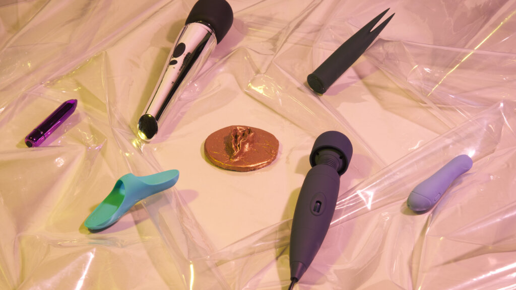 Klitorisvibratorer som ligger på gjennomsiktig plastikk på en beige bakgrunn