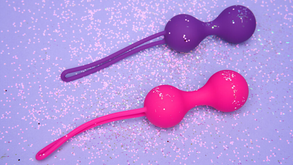 A purple and pink kegel ball on a light purple background with glitter. 