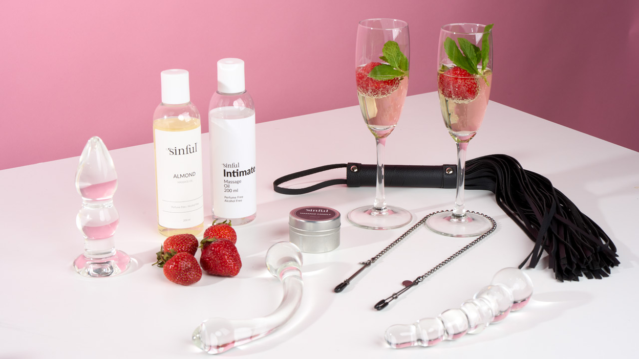 Sexleketøy, massasjeolje, jordbær og champagneglass på et bord